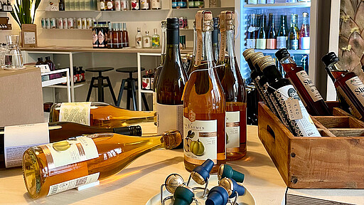 Bewusst genießen im Mindful Drinking Club Ein Tisch auf dem mehrere Flaschen stehen oder liegen. Im Hintergrund sieht man eine kleine Theke mit Barhockern und einen Kühlschrank.